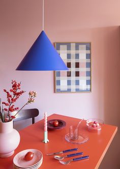 an orange table with plates, utensils and a blue hanging lamp over it