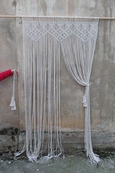 a red umbrella sitting next to a white curtain on the side of a building with tassels hanging from it's sides