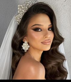 a woman wearing a bridal gown and veil with her hair in the wind, she is looking at the camera