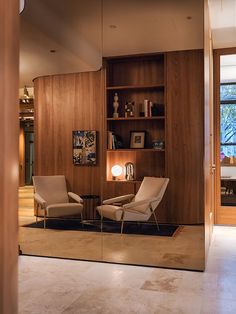 a living room with two chairs and a book shelf on the wall next to it