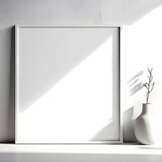 a white vase sitting on top of a shelf next to a blank frame with a plant in it