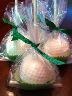 four golf balls wrapped in plastic wrappers on a wooden table with green ribbon around them