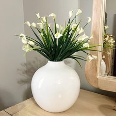 a white vase filled with flowers on top of a wooden table next to a mirror