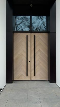 two wooden doors with black handles in front of a white wall and flooring area