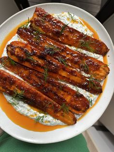 a white plate topped with meat covered in sauce and garnished with green herbs