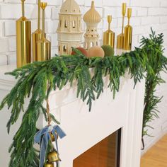 a christmas mantle decorated with pine branches and bells, gold candlesticks and ornaments