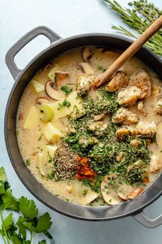 a pot filled with soup and vegetables on top of a blue counter next to fresh herbs