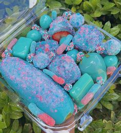 blue and pink treats in a clear container on top of green plants, with sprinkles