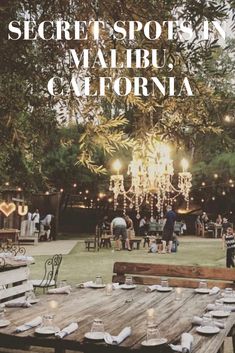 a group of people sitting around a wooden table in the middle of a field with lights strung from trees