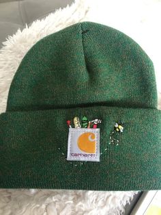 a green beanie hat with an embroidered patch on the front and side of it