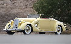 an antique yellow car parked on the side of the road with trees in the background