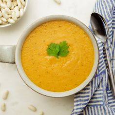 a white bowl filled with carrot soup next to a spoon and some peanuts on the side