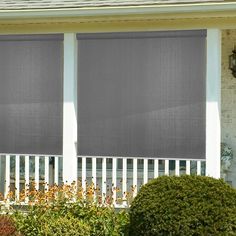 a white house with two windows covered in gray shades and bushes outside the window,