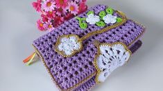 a purple crocheted purse with flowers on it and a pink flower in the background