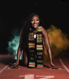 a woman kneeling down on a running track with her hands in the air while wearing a colorful scarf