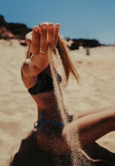 a woman sitting on top of a sandy beach next to the ocean with her hands in the air