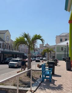 people are walking down the sidewalk in front of shops and palm trees on a sunny day