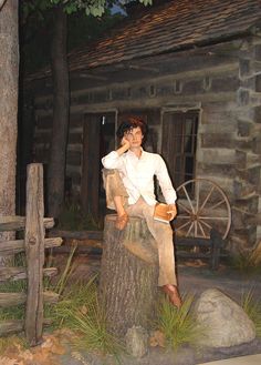 a fake man sitting on top of a tree stump next to a building and fence