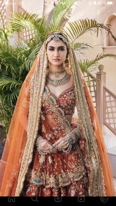 a woman in an orange and gold bridal gown standing next to a palm tree