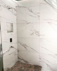 a bathroom with white marble walls and flooring, including a shower head in the corner