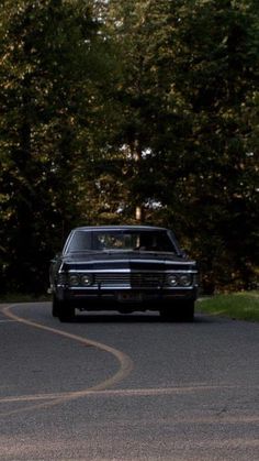 a black car driving down a curvy road in front of some tall trees