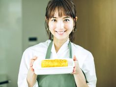 a woman in an apron holding a white plate with food on it and smiling at the camera