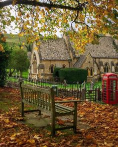 a wooden bench sitting next to a red phone booth on top of a leaf covered field