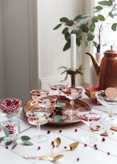 a table topped with lots of glasses filled with liquid and goldware next to a potted plant