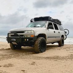 a white truck parked on top of a sandy beach next to the ocean in front of an overcast sky