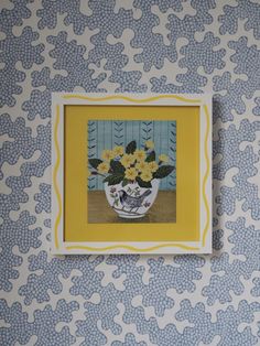 a vase with yellow flowers on a blue and white wallpapered background is framed