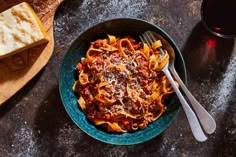 a bowl of pasta with meat sauce and bread on a table next to a glass of wine