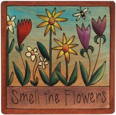 a wooden plaque with flowers and the words smell the flowers written in black on it