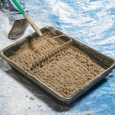 a person is shoveling sand into a metal pan on a blue tarp covered surface