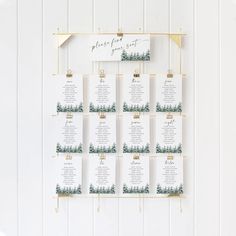 a wedding seating chart hanging on a wall with pine trees and greenery in the background