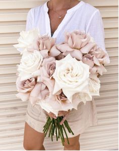 a woman holding a bouquet of white and pink flowers in her hands while standing next to a building