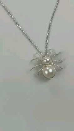 a silver necklace with a white pearl spider charm on it's back and two pearls in the middle