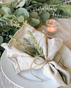 a white plate topped with a napkin covered in greenery next to a lit candle