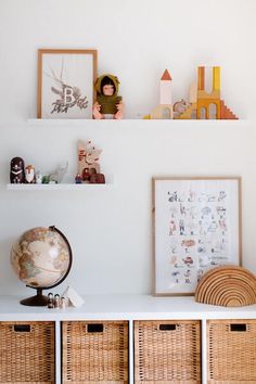 a shelf with baskets and toys on top of it next to a wall mounted art piece