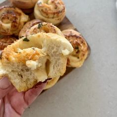 a person holding a piece of bread in their hand with other pastries on the table