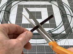 a pair of scissors being used to cut wire on a piece of paper with holes in the middle