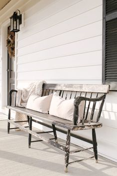 a wooden bench sitting on the side of a white house next to a lamp post