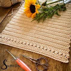 crocheted placemat with sunflower and scissors on wooden table next to yarn