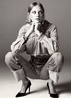 a black and white photo of a woman in high heels sitting on the floor with her hands under her chin