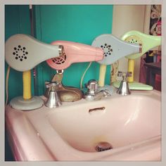 a pink sink with three hair dryers on it's faucet and soap dispenser