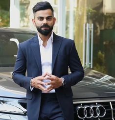 a man in a suit standing next to an audi car with his hands on his chest