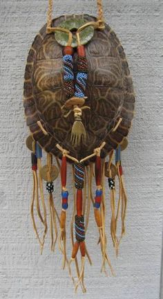 a decorative wall hanging made out of shells and feathers with beads on the bottom, attached to a white brick wall