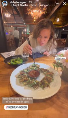 a woman sitting at a table in front of a white plate with food on it