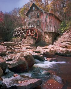 an old mill sits on the edge of a river with rocks in front of it