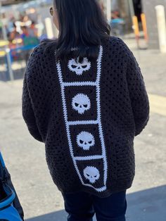 a woman is walking down the street with her back to the camera and wearing a black sweater with skulls on it