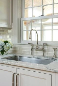 a white kitchen with marble counter tops and stainless steel faucet, window over the sink